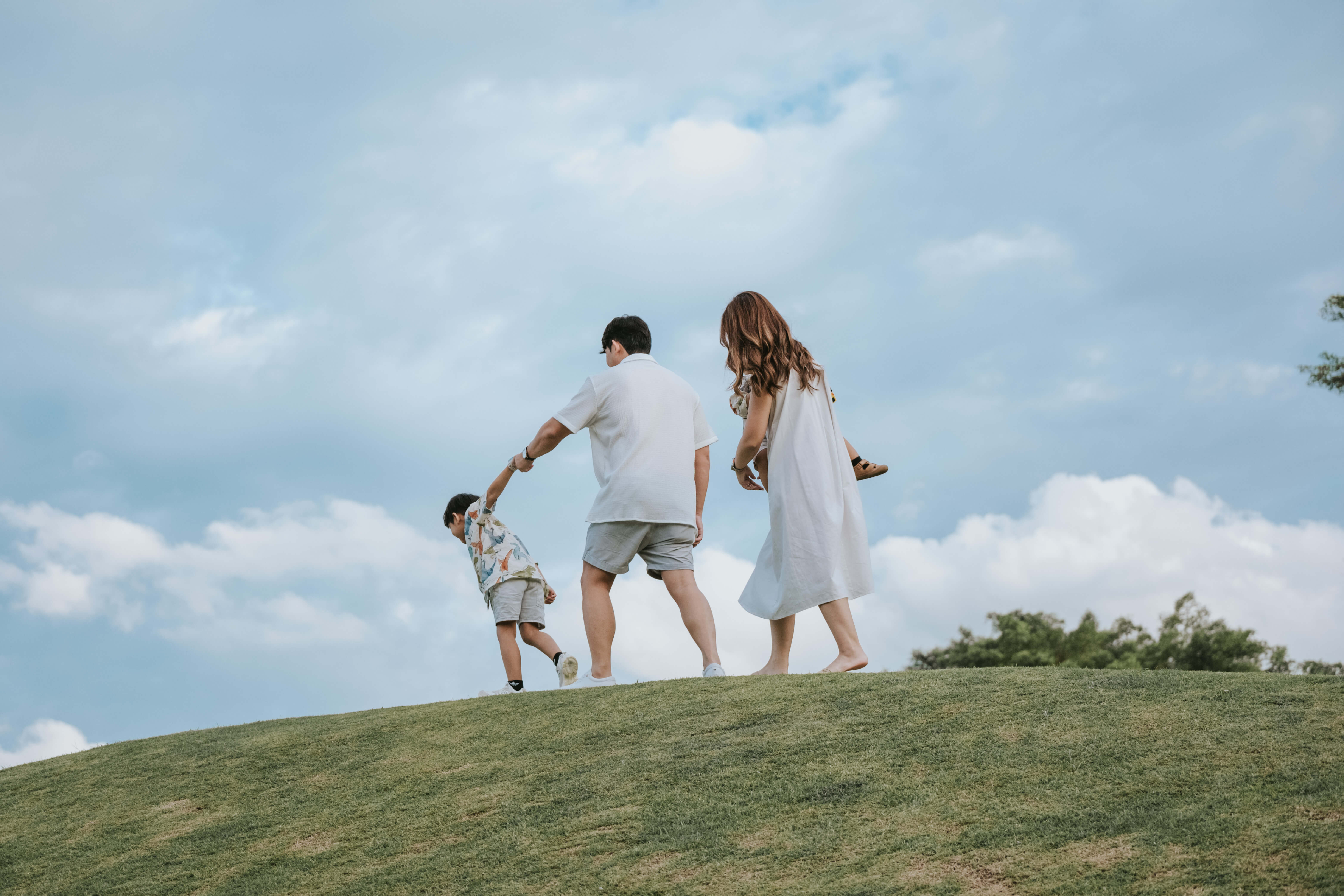 kid holding dad's hands and pulling him on a hill